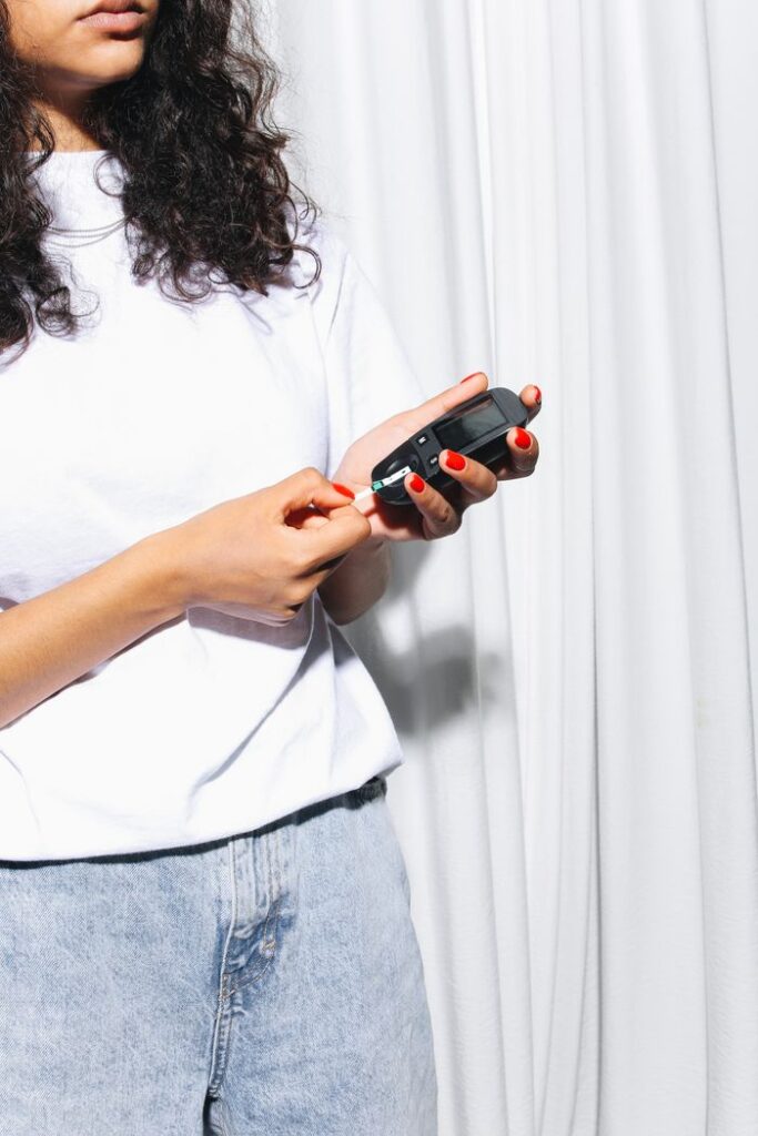 A woman uses a glucometer to test her blood sugar levels while standing indoors.