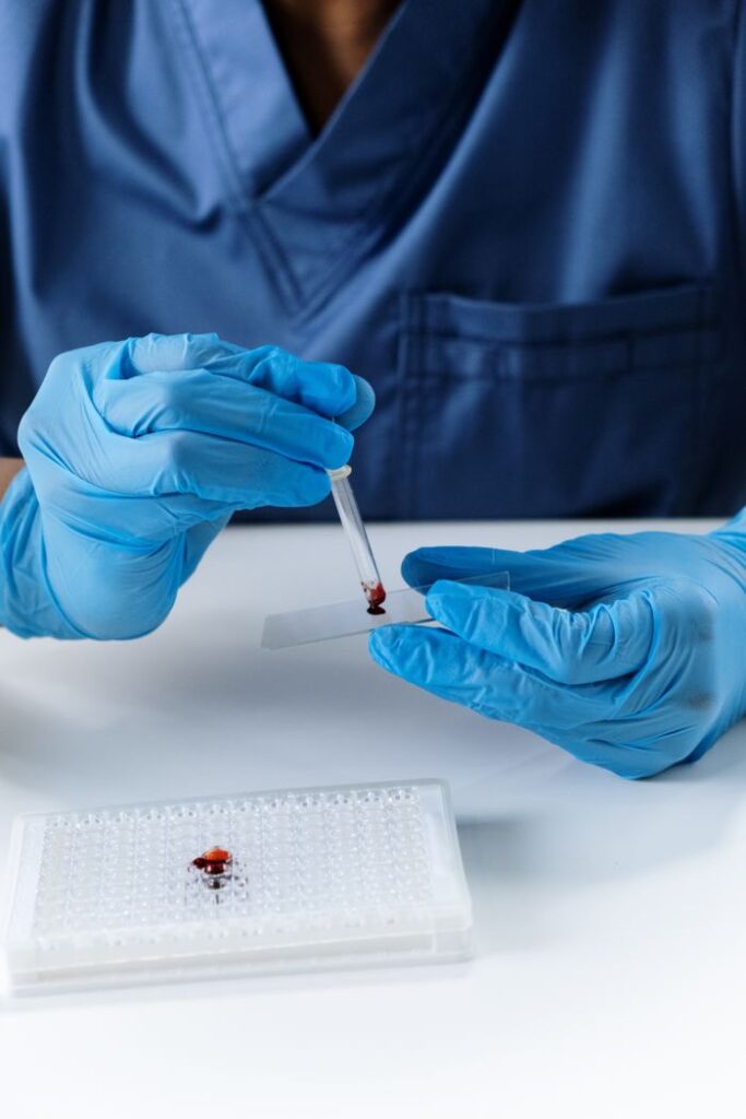 A scientist in blue gloves using a dropper to place a blood sample on a microscope slide indoors.