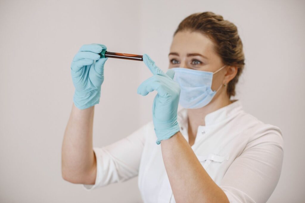 Crafting Captivating Headlines: Your awesome post title goes here A female healthcare worker wearing gloves and a mask examines a blood sample in a test tube.