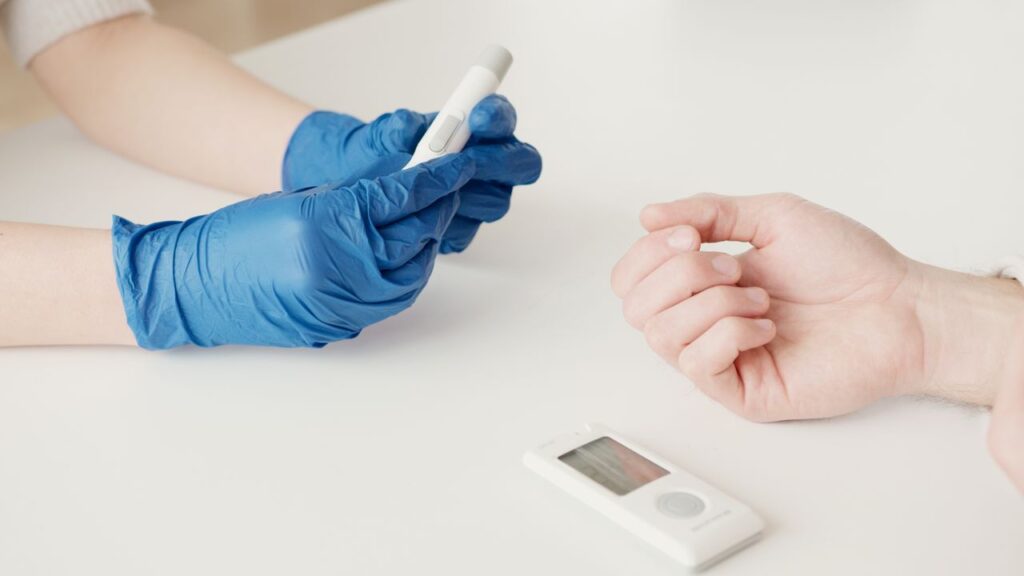 A healthcare worker uses a glucometer to check blood sugar levels in an indoor setting.