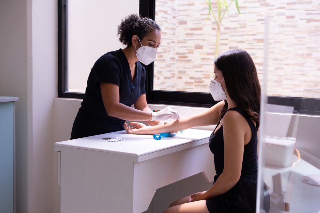 The Art of Drawing Readers In: Your attractive post title goes here A healthcare professional wearing a face mask performs a blood test on a female patient in a clinic.