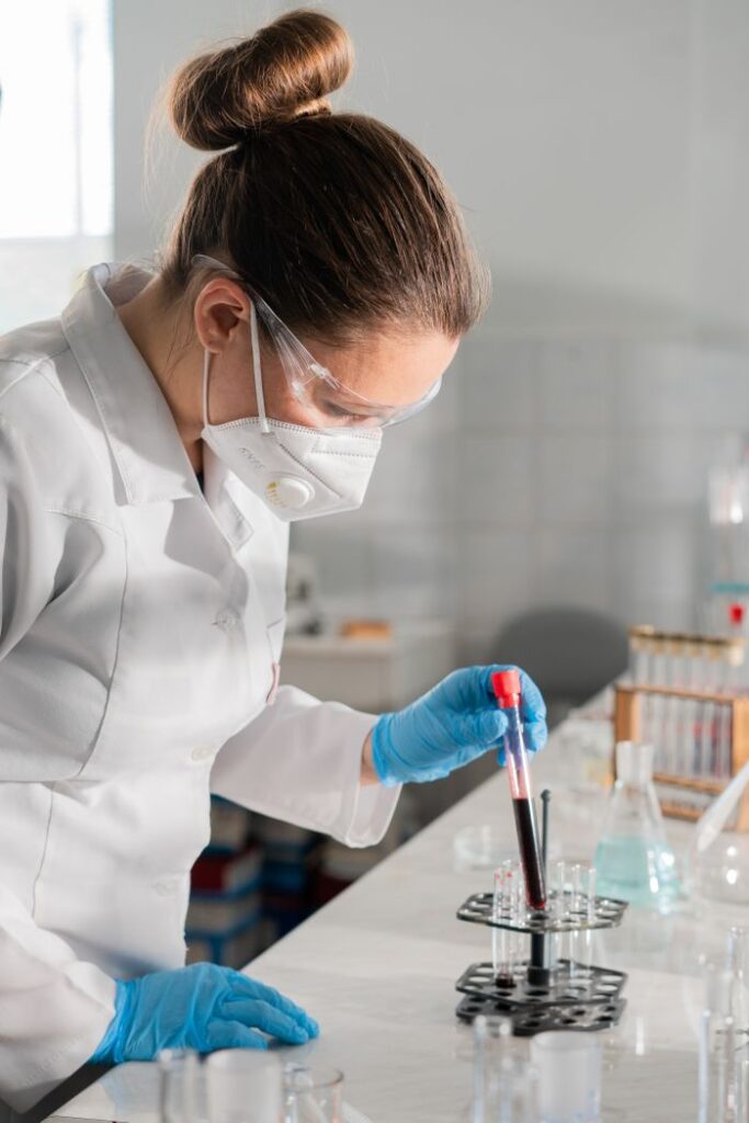 Woman in protective gear analyzing blood sample in a laboratory setting.